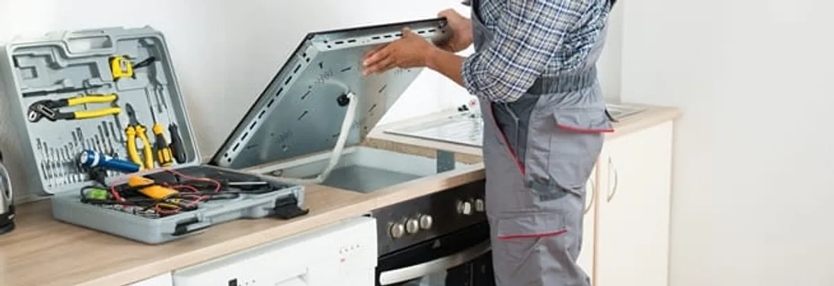 Cooktop repair technician lifting a built-in stovetop for service in Grand Rapids, MI