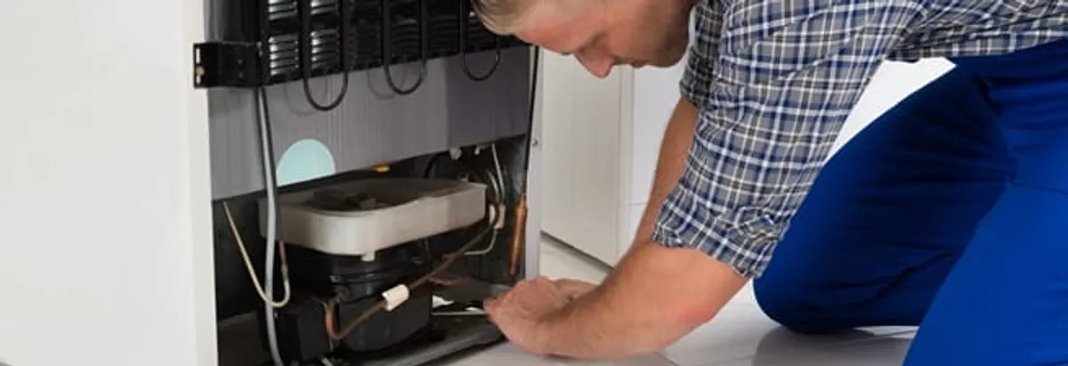 Refrigerator repair technician servicing the compressor and condenser area in Grand Rapids, MI